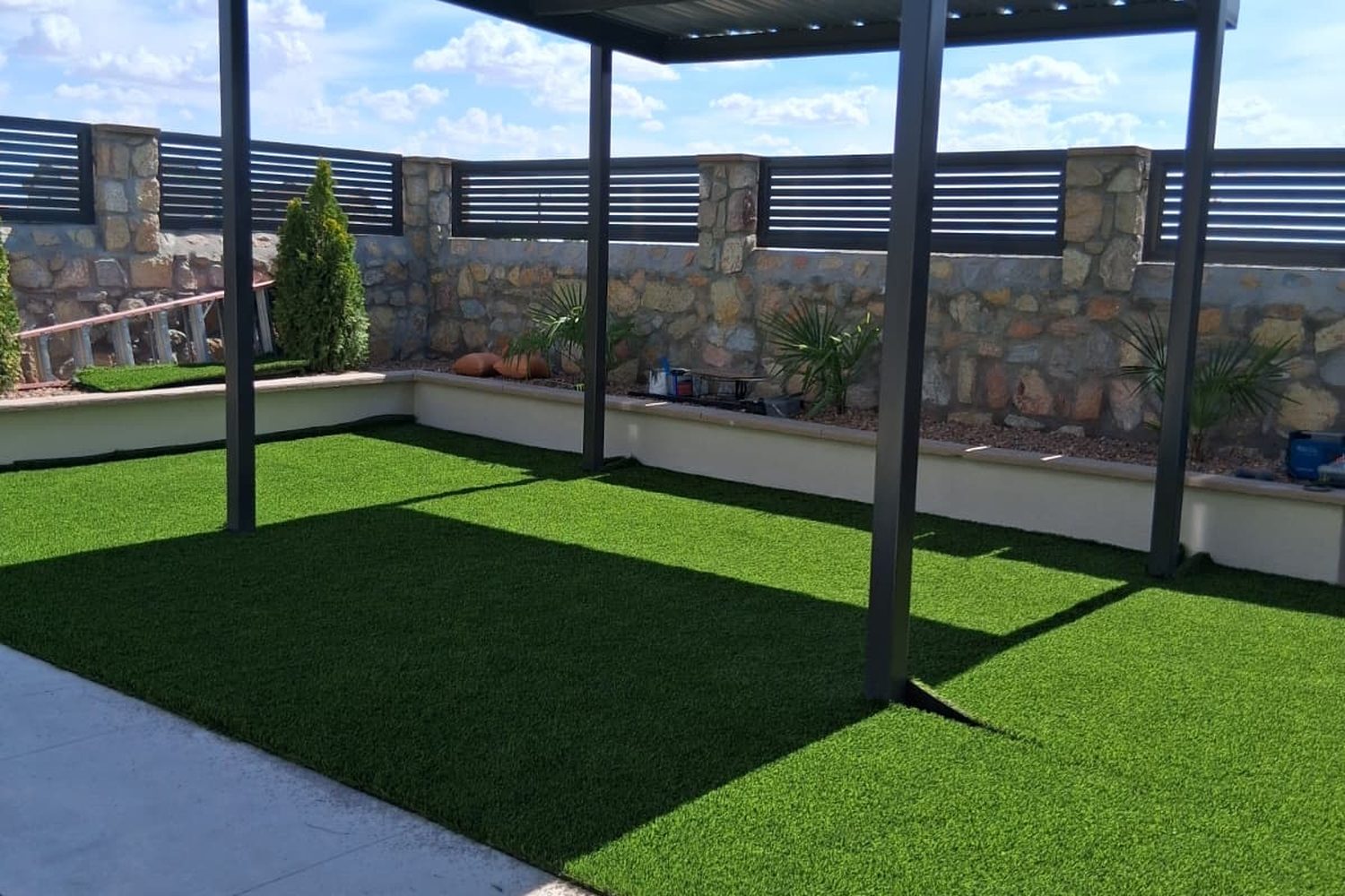 Artificial turf under a black steel pergola beside a pool
