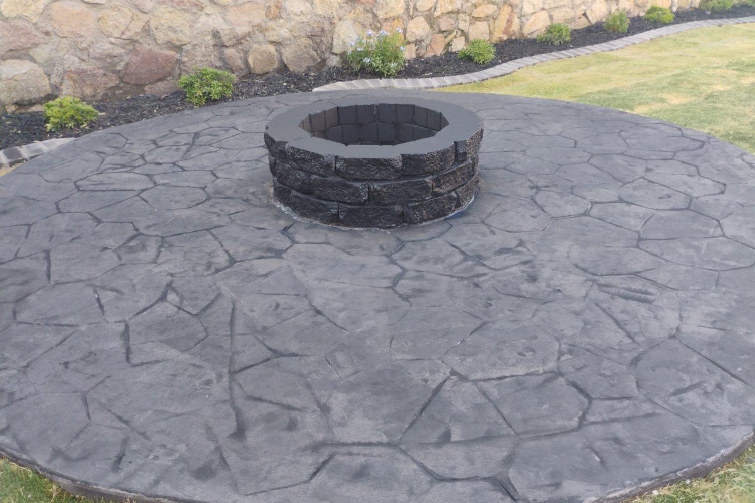 Stamped concrete fire pit area with a rock wall behind it